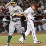 Oakland Athletics' Billy Burns, left, scores a run on a double hit by teammate Mark Canha off Arizona Diamondbacks pitcher Chase Anderson, right, during the third inning of a baseball game Friday, Aug. 28, 2015, in Phoenix. (AP Photo/Ross D. Franklin)