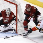 Calgary Flames' Matt Stajan (18) tries to get a shot off as he is shoved to the ice by Arizona Coyotes' Michael Stone (26) as Coyotes goalie Louis Domingue, left, protects the net during the second period of an NHL hockey game Friday, Feb. 12, 2016, in Glendale, Ariz. (AP Photo/Ross D. Franklin)