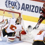 Calgary Flames' Joni Ortio, left, of Finland, makes a save on a shot as Arizona Coyotes' Max Domi (16) tries to get at the puck while Flames' Mark Giordano (5) watches during the third period of an NHL hockey game Monday, March 28, 2016, in Glendale, Ariz.  The Flames defeated the Coyotes 5-2. (AP Photo/Ross D. Franklin)