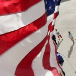 Fans walk through a concourse under a United States flag during the seventh inning of a spring training baseball game between the Seattle Mariners and the Arizona Diamondbacks, Monday, March 7, 2016, in Peoria, Ariz. (AP Photo/Charlie Riedel)