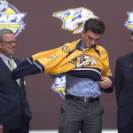 Dante Fabbro, enter, puts on his sweater as he stands with members of the Nashville Predators management team at the NHL draft in Buffalo, N.Y., Friday June 24, 2016. (Nathan Denette/The Canadian Press via AP) MANDATORY CREDIT