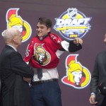 Logan Brown pulls on his sweater as he stands on stage with members of the Ottawa Senators management team at the NHL hockey draft, Friday, June 24, 2016, in Buffalo, N.Y. (Nathan Denette/The Canadian Press via AP)