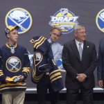 Alexander Nylander, eighth overall pick, puts on his sweater as he stands on stage with members of the Buffalo Sabres management team at the NHL hockey draft, Friday, June 24, 2016, in Buffalo, N.Y. (Nathan Denette/The Canadian Press via AP)