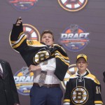 Charlie McAvoy, second from left, puts on his sweater as he stands on stage with members of the Boston Bruins management team and others at the NHL draft in Buffalo, N.Y., Friday June 24, 2016. (Nathan Denette/The Canadian Press via AP) MANDATORY CREDIT