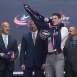 Pierre-Luc Dubois, second from right, third overall pick, puts on his sweater as he stands with members of the Columbus Blue Jackets management team at the NHL draft in Buffalo, N.Y., Friday June 24, 2016. (Nathan Denette/The Canadian Press via AP) MANDATORY CREDIT
