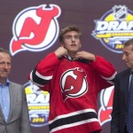 Michael McLeod, center, puts on his sweater as he stands with members of the New Jersey Devils management team and others at the NHL draft in Buffalo, N.Y., Friday June 24, 2016. (Nathan Denette/The Canadian Press via AP) MANDATORY CREDIT