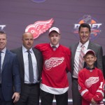 Dennis Cholowski, center, stands on stage with members of the Detroit Red Wings management team and others at the NHL draft in Buffalo, N.Y., Friday June 24, 2016. (Nathan Denette/The Canadian Press via AP) MANDATORY CREDIT