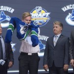 Olli Juolevi, second from left, fifth overall pick, puts on his sweater as he stands with members of the Vancouver Canucks management team at the NHL draft in Buffalo, N.Y., Friday June 24, 2016. (Nathan Denette/The Canadian Press via AP) MANDATORY CREDIT