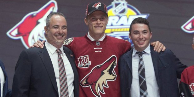 Jakob Chychrun stands on stage with members of the Arizona Coyotes management team at the NHL hocke...