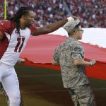 Arizona Cardinals wide receiver Larry Fitzgerald (11) adjusts the hat of one of the people holding the flag during the national anthem before an NFL football game between the San Francisco 49ers and the Cardinals in Santa Clara, Calif., Thursday, Oct. 6, 2016. (AP Photo/Ben Margot)