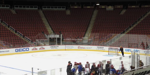 A group of Arizona Coyotes players gather and listen to assistant coach Jim Playfair explain a dril...