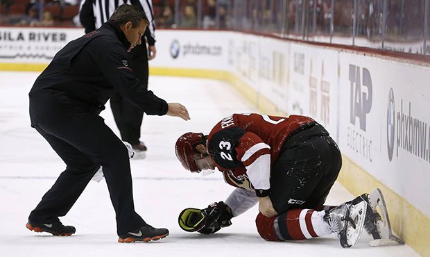 Arizona Coyotes' Oliver Ekman-Larsson (23) grabs his left knee as a Coyotes trainer arrives to help...