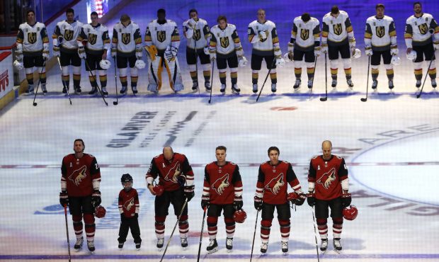 Members of the Arizona Coyotes, foreground, and the Vegas Golden Knights pause for a moment of sile...