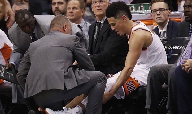 Phoenix Suns guard Devin Booker is helped on the bench after coming out of the NBA basketball game ...