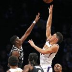 Brooklyn Nets guard Caris LeVert (22) defends as Phoenix Suns guard Devin Booker (1) shoots a three-point shot in the first half of an NBA basketball game, Tuesday, Oct. 31, 2017, in New York. Booker had 32 points to lead the Suns to a 122-114 victory over the Nets. (AP Photo/Kathy Willens)