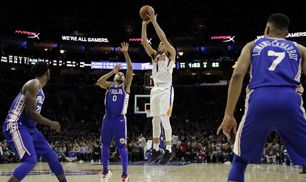 Phoenix Suns' Devin Booker (1) goes up for a shot past Philadelphia 76ers' Joel Embiid (21), Jerryd...