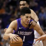 Phoenix Suns guard Devin Booker (1) is grabbed by New York Knicks guard Courtney Lee during the second half of an NBA basketball game Friday, Jan. 26, 2018, in Phoenix. The Knicks defeated the Suns 107-85. (AP Photo/Rick Scuteri)