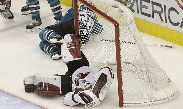 Arizona Coyotes goaltender Scott Wedgewood, bottom, grabs his helmet after being hit during the thi...