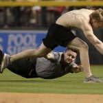 A fan, top, is tackled by security after running onto the field during the third inning of a baseball game between the Colorado Rockies and the Arizona Diamondbacks, Thursday, March 29, 2018, in Phoenix. (AP Photo/Matt York)