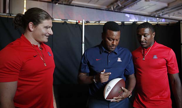 Flanked by linebacker Colin Schooler, left, and quarterback Khalil Tate, Arizona coach Kevin Sumlin...