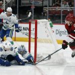 Arizona Coyotes center Nick Cousins (25) shoots on goal as Vancouver Canucks left wing Antoine Roussel (26) and goaltender Anders Nilsson defend the net in the second period during an NHL hockey game, Thursday, Oct. 25, 2018, in Glendale, Ariz. (AP Photo/Rick Scuteri)