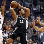 San Antonio Spurs guard Bryn Forbes (11) passes over Phoenix Suns guard Devin Booker, right, and forward Mikal Bridges (25) during the first half of an NBA basketball game, Wednesday, Nov. 14, 2018, in Phoenix. (AP Photo/Matt York)
