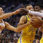 Golden State Warriors guard Stephen Curry (30) drives between Phoenix Suns' Devin Booker (1) and Deandre Ayton during the first half of an NBA basketball game Monday, Dec. 31, 2018, in Phoenix. (AP Photo/Rick Scuteri)