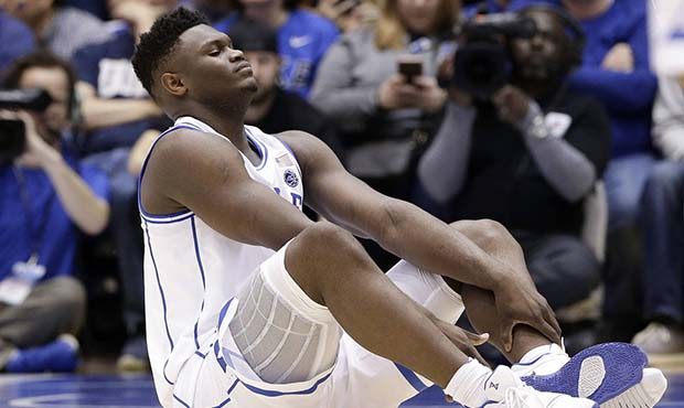 Duke's Zion Williamson sits on the floor following a injury during the first half of an NCAA colleg...