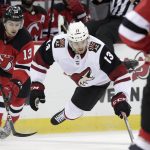 Arizona Coyotes center Vinnie Hinostroza, right, goes airborne while competing for the puck with New Jersey Devils center Nico Hischier, of Switzerland, during the first period of an NHL hockey game, Saturday, March 23, 2019, in Newark, N.J. (AP Photo/Julio Cortez)