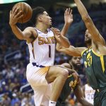 Phoenix Suns guard Devin Booker (1) shoots as Utah Jazz center Rudy Gobert (27) and forward Royce O'Neale (23) defend during the first half of an NBA basketball Wednesday, April 3, 2019, in Phoenix. (AP Photo/Ross D. Franklin)