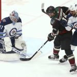 Winnipeg Jets goaltender Connor Hellebuyck (37) makes a save on a shot by Arizona Coyotes center Brad Richardson (15) as Winnipeg Jets defenseman Dustin Byfuglien (33) gives Richardson a push during the second period of an NHL hockey game Saturday, April 6, 2019, in Glendale, Ariz. (AP Photo/Ross D. Franklin)