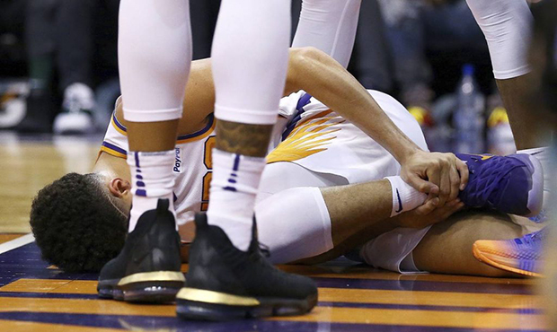 An injured Phoenix Suns guard Devin Booker holds his ankle after turning it during the first half o...