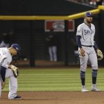 San Diego Padres shortstop Fernando Tatis Jr., right, pauses with the baseball after making a fielding error on a ball hit by Arizona Diamondbacks' Adam Jones, as Padres third baseman Manny Machado (13) kneels after making a diving attempt for the grounder during the sixth inning of a baseball game Saturday, April 13, 2019, in Phoenix. (AP Photo/Ross D. Franklin)