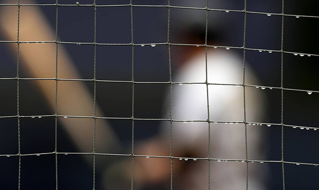 Rainwater drops hang from the netting as Pittsburgh Pirates' Colin Moran, behind, bats during the f...