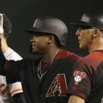 Arizona Diamondbacks' Domingo Leyba, middle, smiles while acknowledging his teammates in the dugout after getting his first in the majors, as Diamondbacks first base coach Dave McKay, right, and San Francisco Giants first baseman Brandon Belt, left, stand nearby during the sixth inning of a baseball game Saturday, June 22, 2019, in Phoenix. (AP Photo/Ross D. Franklin)