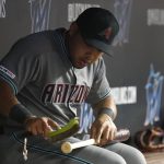 Arizona Diamondbacks' Yasmany Tomas brushes off a bat while sitting in the dugout during the fifth inning of a baseball game against the Miami Marlins, Friday, July 26, 2019, in Miami. The 28-year-old outfielder was brought back from the minor leagues by the Diamondbacks on Friday. (AP Photo/Wilfredo Lee)
