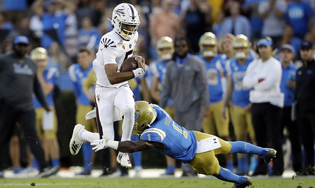 Arizona State quarterback Jayden Daniels, left, leaps over UCLA defensive back Darnay Holmes (1) du...