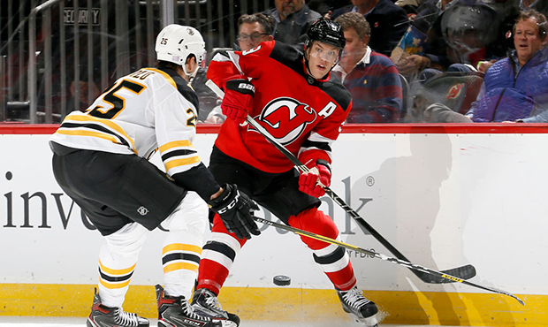 Taylor Hall #9 of the New Jersey Devils pass the puck as Brandon Carlo #25 of the Boston Bruins tri...