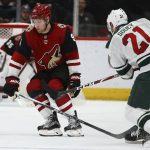 Minnesota Wild defenseman Carson Soucy (21) sends a shot past Arizona Coyotes left wing Taylor Hall during the second period of an NHL hockey game Thursday, Dec. 19, 2019, in Glendale, Ariz. (AP Photo/Ross D. Franklin)