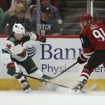 Arizona Coyotes left wing Taylor Hall (91) sends the puck past Minnesota Wild left wing Kevin Fiala (22) during the first period of an NHL hockey game Thursday, Dec. 19, 2019, in Glendale, Ariz. (AP Photo/Ross D. Franklin)