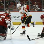 Calgary Flames left wing Johnny Gaudreau (13) kicks the puck as Arizona Coyotes defenseman Jakob Chychrun (6) helps out Coyotes goaltender Antti Raanta (32) during the first period of an NHL hockey game, Tuesday, Dec. 10, 2019 in Glendale, Ariz. (AP Photo/Ross D. Franklin)