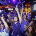 Justin Rogstad, center, cheers on LSU against Clemson in the NCAA College Football Playoff championship game, while watching on screens at Fred's Bar & Grill, in Baton Rouge, La., Monday, Jan. 13, 2020. (AP Photo/Brett Duke)