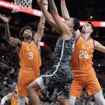 San Antonio Spurs' Trey Lyles, center, attempts to shoot against Phoenix Suns' Kelly Oubre, Jr. (3) and Dario Saric during the first half of an NBA basketball game, Friday, Jan. 24, 2020, in San Antonio. (AP Photo/Darren Abate)