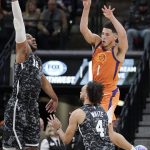 Phoenix Suns' Devin Booker (1) passes the ball as he is defended by San Antonio Spurs' LaMarcus Aldridge (12) and Derrick White during the first half of an NBA basketball game, Friday, Jan. 24, 2020, in San Antonio. (AP Photo/Darren Abate)