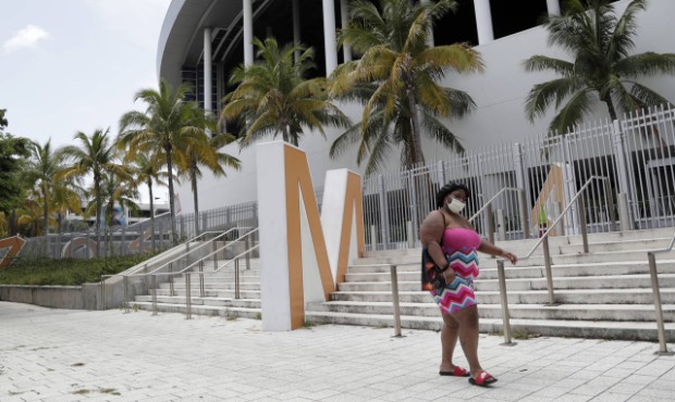A woman wearing a protective face covering walks past Marlins Park, Monday, July 27, 2020, in Miami...