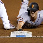 Logos on first base and the jersey sleeve pay tribute to Jackie Robinson Day as San Francisco Giants' Mike Yastrzemski dives back safely on a pick-off attempt against the Arizona Diamondbacks during the third inning of a baseball game, Friday, Aug. 28, 2020, in Phoenix. (AP Photo/Matt York)
