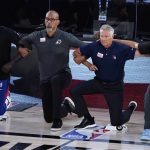 Phoenix Suns head coach Monty Williams, center left, and Philadelphia 76ers head coach Brett Brown, center right, kneel during the national anthem prior to the start of an NBA basketball game Tuesday, Aug. 11, 2020, in Lake Buena Vista, Fla. (AP Photo/Ashley Landis, Pool)