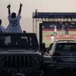 Mike Kim, left, and Jacob Zelaya cheer in their vehicle outside Dodger Stadium and watch the television broadcast of Game 1 of the 2020 World Series between the Los Angeles Dodgers and the Tampa Bay Rays in Tuesday, Oct. 20, 2020, in Los Angeles. Due to the spread of COVID-19, all of the 2020 World Series games will be played in Arlington, Texas. (AP Photo/Ashley Landis)