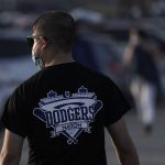 A baseball fan walks back to his car outside Dodger Stadium while watching the television broadcast of Game 1 of the 2020 World Series between the Los Angeles Dodgers and the Tampa Bay Rays in Tuesday, Oct. 20, 2020, in Los Angeles. Due to the spread of COVID-19, all of the 2020 World Series games will be played in Arlington, Texas. (AP Photo/Ashley Landis)