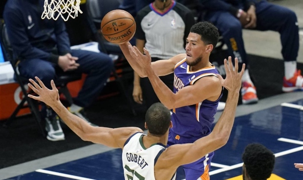 Phoenix Suns guard Devin Booker, rear, passes the ball as Utah Jazz center Rudy Gobert (27) defends...
